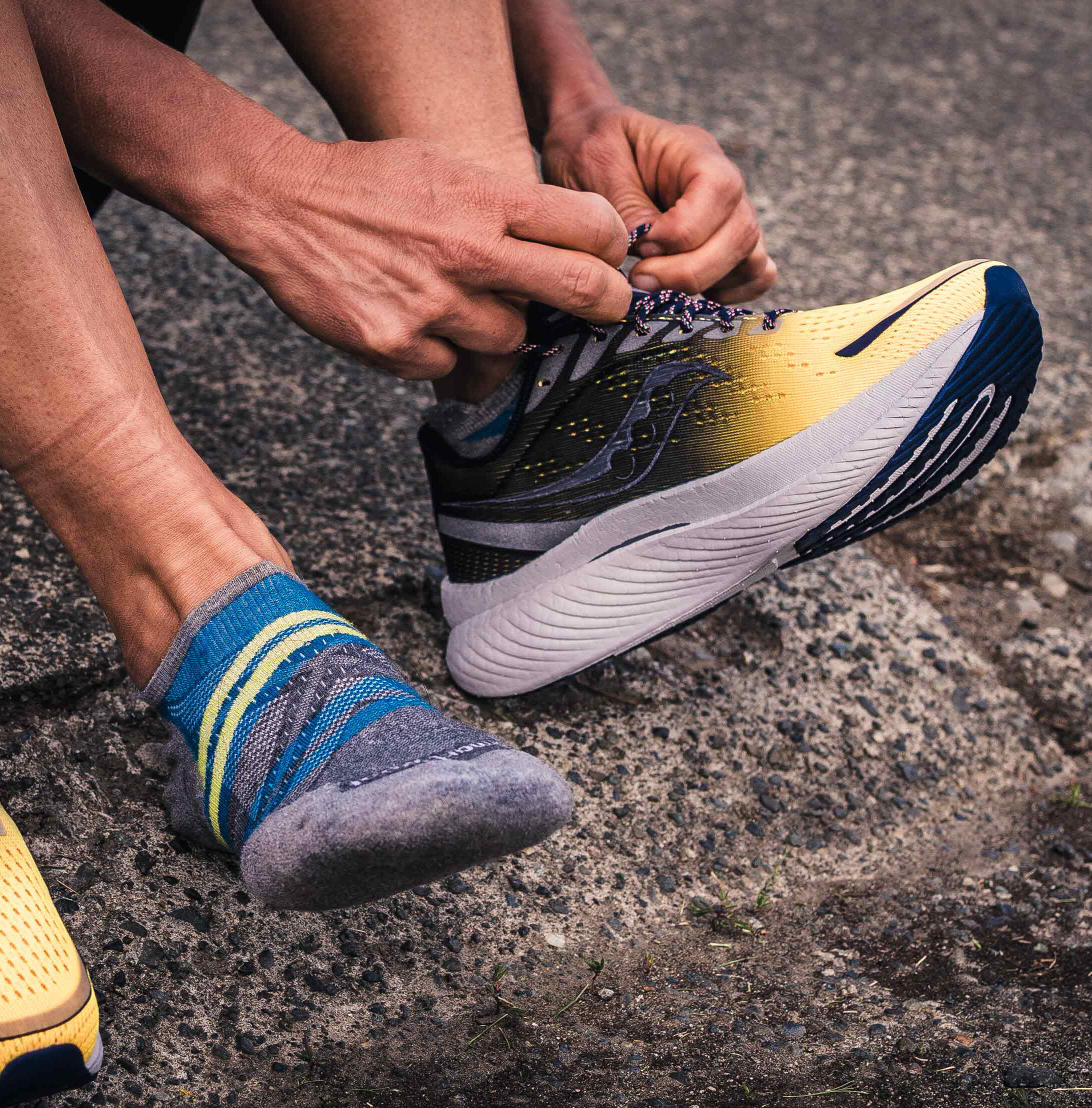 Close-up of a runner tying yellow and black Saucony running shoes on a paved trail, preparing for a run in comfortable footwear.